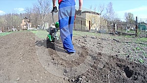 Man cultivates the ground in the garden with a tiller, preparing the soil for sowing