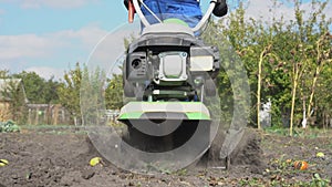 Man cultivates the ground in the garden with a tiller, preparing the soil for sowing