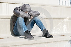 Man curled up sitting on an outdoor stairway