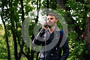 A man with a curly beard in a black jacket thoughtfully looks into the distance while talking on a smartphone