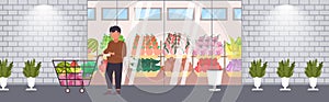 Man customer pushing trolley cart with groceries vegetables and fruits shopping concept modern grocery shop supermarket