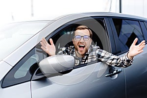 Man customer sitting in car salon and smiling, choosing auto and wanting to buy new automobile in showroom dealership store. Car