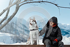 Man and Cute Siberian Husky dog sitting on bench highly in mountains