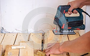 A man cuts a board with an electric saw. Repair of the floor in the house. Selective focus