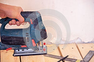 A man cuts a board with an electric saw. Repair of the floor in the house. Selective focus