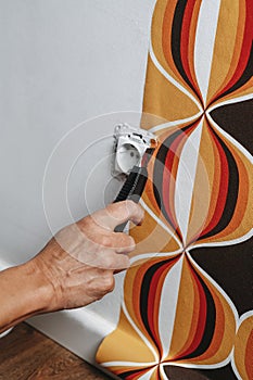 man cuts the edges of a wallpaper around a socket