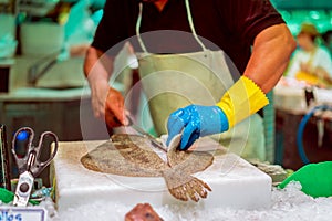 A man cuts fish turbot before selling at a fish market. Bright colours, selective focus, bokeh