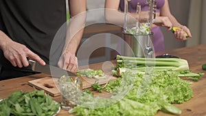 Man cuts fresh celery on a cutting Board at the home kitchen. Woman helping cooking vegetable cocktail