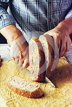 A man cuts freshly baked whole-wheat bran bread with a sharp knife