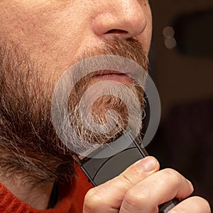 A man cuts his gray beard trimmer