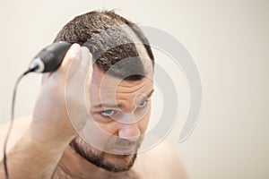 A man cuts his head with a clipper, self-shaving his head baldly photo