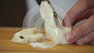 A man cuts mozzarella cheese with a knife on a wooden board.