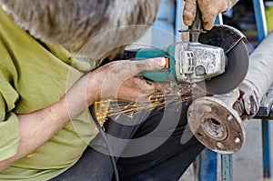 A man cuts off the lock washers from the cross of the cardan shaft of an automobile with an angle grinder.