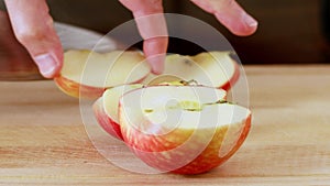 Man cuts red apple with kitchen knife on wooden board