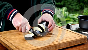 Man cuts slices eggplant on cutting board.