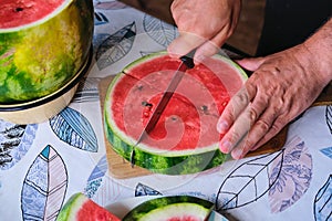 A man cuts a watermelon circle into triangular segments on a board on a plastic-covered table