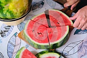 A man cuts a watermelon circle into triangular segments on a board on a plastic-covered table