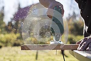 Man cuts wood product using an electric jigsaw joinery in the sun on a warm summer day.