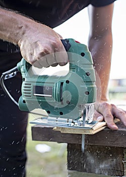 Man cuts wood products, using electric jigsaws outdoors