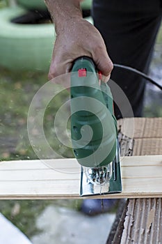 Man cuts wood products, using electric jigsaws outdoors