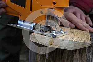 Man cuts wood products, using electric jigsaws outdoors. Close-up