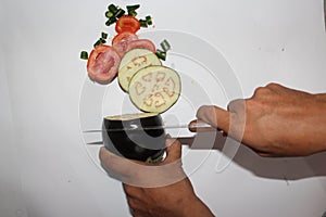 Man cutting eggplant tomatoes and hot pepper on white background