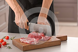 Man cutting fresh raw meat on wooden board in kitchen