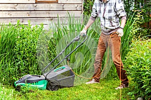 Man cutting green grass with lawn mower in backyard