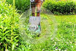 Man cutting green grass with lawn mower in backyard