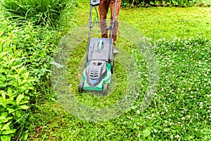 Man cutting green grass with lawn mower in backyard