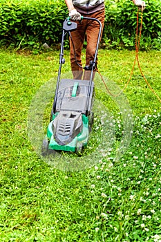 Man cutting green grass with lawn mower in backyard