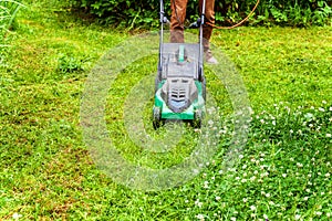 Man cutting green grass with lawn mower in backyard