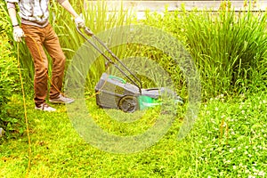 Man cutting green grass with lawn mower in backyard. Gardening country lifestyle background. Beautiful view on fresh green grass