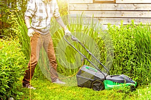 Man cutting green grass with lawn mower in backyard. Gardening country lifestyle background. Beautiful view on fresh green grass