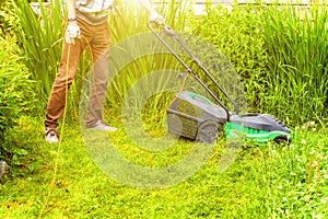 Man cutting green grass with lawn mower in backyard. Gardening country lifestyle background. Beautiful view on fresh green grass