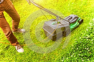 Man cutting green grass with lawn mower in backyard. Gardening country lifestyle background. Beautiful view on fresh green grass