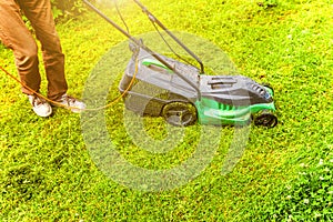 Man cutting green grass with lawn mower in backyard. Gardening country lifestyle background. Beautiful view on fresh green grass