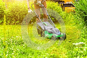 Man cutting green grass with lawn mower in backyard. Gardening country lifestyle background. Beautiful view on fresh green grass