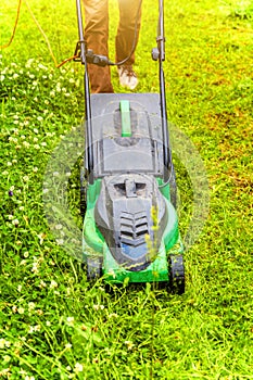 Man cutting green grass with lawn mower in backyard. Gardening country lifestyle background. Beautiful view on fresh green grass