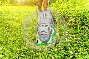 Man cutting green grass with lawn mower in backyard. Gardening country lifestyle background. Beautiful view on fresh green grass