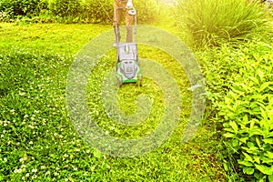 Man cutting green grass with lawn mower in backyard. Gardening country lifestyle background. Beautiful view on fresh green grass