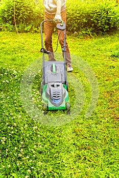 Man cutting green grass with lawn mower in backyard. Gardening country lifestyle background. Beautiful view on fresh green grass