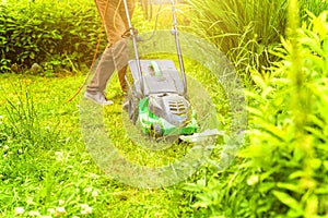 Man cutting green grass with lawn mower in backyard. Gardening country lifestyle background. Beautiful view on fresh green grass