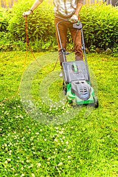 Man cutting green grass with lawn mower in backyard. Gardening country lifestyle background. Beautiful view on fresh green grass