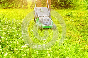 Man cutting green grass with lawn mower in backyard. Gardening country lifestyle background. Beautiful view on fresh green grass