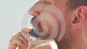 Man cutting his own beard and mustache with scissors and comb. Caucasian red bearded male trimming hair on face at home.