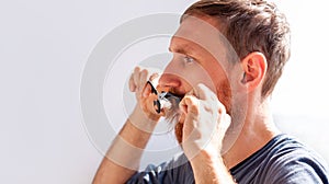 Man cutting his own beard and mustache with scissors and comb. Caucasian red bearded male trimming hair on face at home