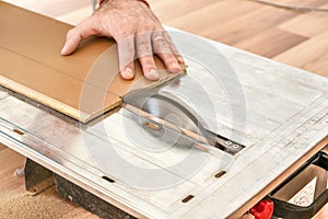 Man cutting laminate floor boards on circular saw, detail on hands holding wooden panel