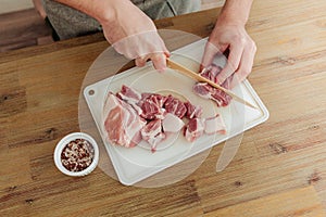 Man cutting meat with a knife on a cutting board. Wooden table. Fresh pork meat. Top view