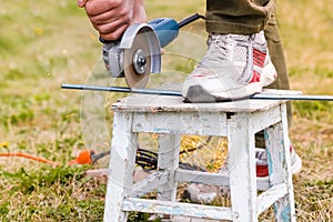 Man cutting metal tack by electric angle grinder, working process